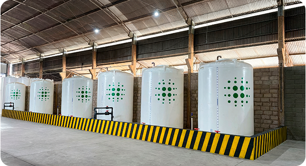 Fileira de tanques de armazenamento brancos com marca Greon, área industrial com faixa de segurança amarela e preta.